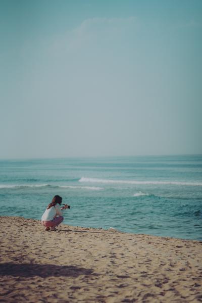 女孩蹲在沙滩上拍大海